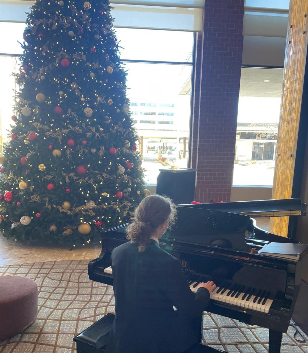 Student Playing a piano in front of a christmas tree